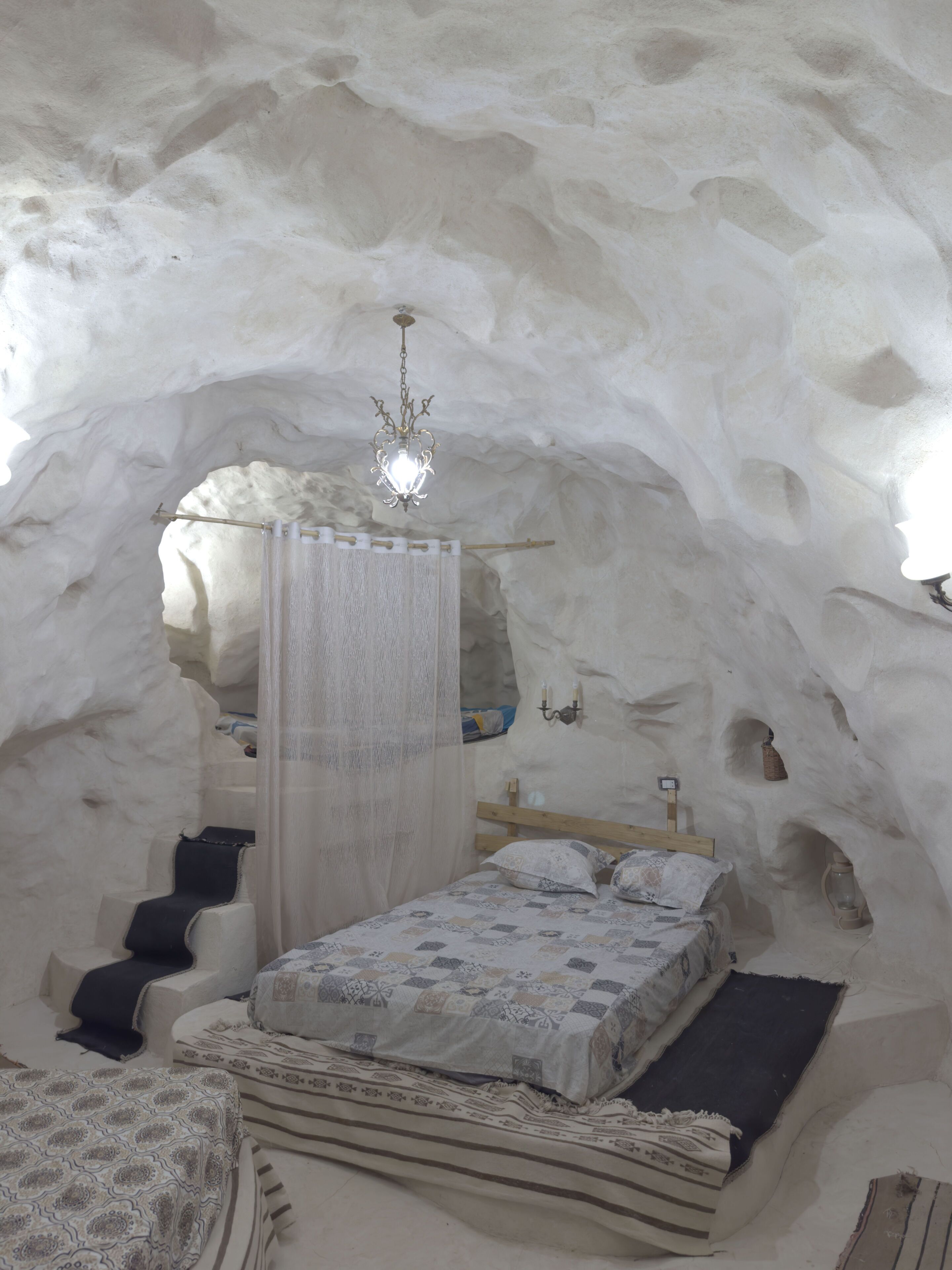 Une chambre aménagée dans une grotte de glace, avec un lit, un luminaire suspendu et un banc en bois.