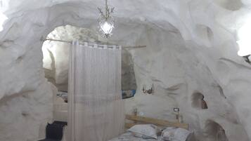 Une chambre aménagée dans une grotte de glace, avec un lit, un luminaire suspendu et un banc en bois.