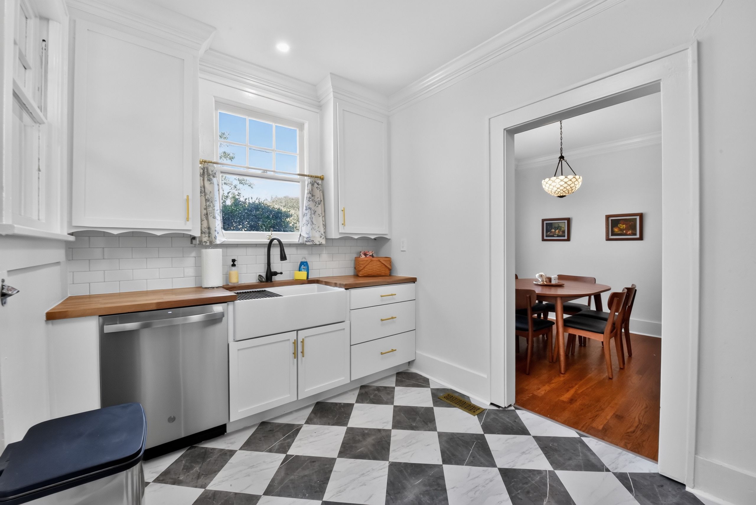A compact kitchen with white cabinetry, a checkered floor, and a dining area with a wooden table and chairs.