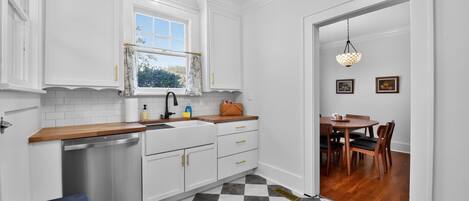 A compact kitchen with white cabinetry, a checkered floor, and a dining area with a wooden table and chairs.