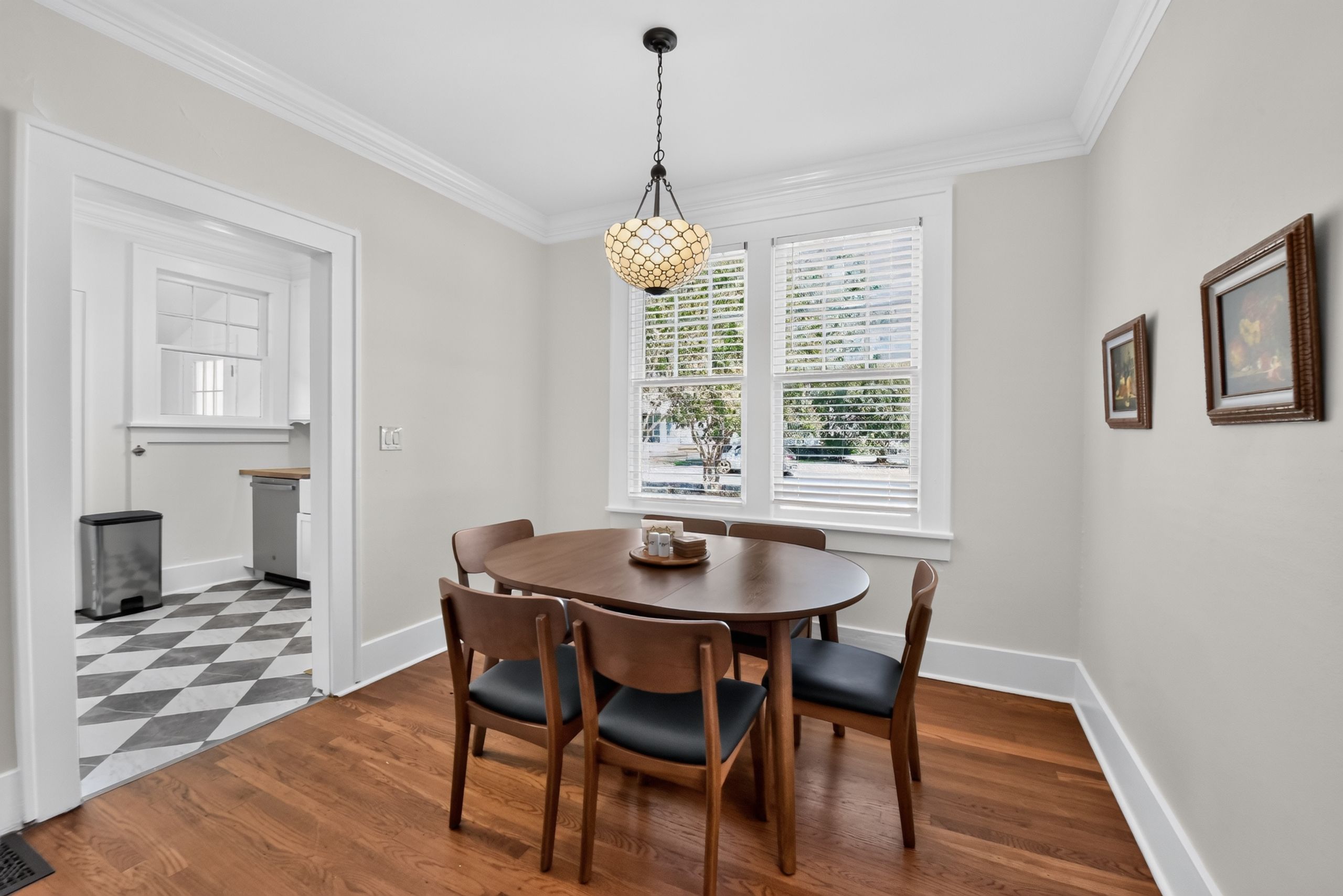 A dining area with a round table and chairs, a chandelier, and a view of the outdoors through large windows.
