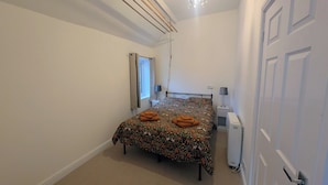 Un dormitorio con cama, ventana, radiador y puerta.