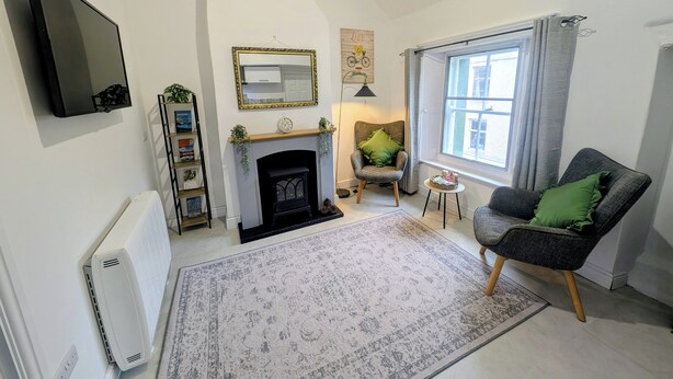 Una sala de estar con chimenea, televisor montado en la pared, estantería y ventana con cortinas.
