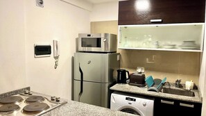 A compact kitchen with a microwave, refrigerator, washing machine, and a small countertop with a sink and dish rack. - Bright Studio Apartment in the Heart of Palermo (Buenos Aires)