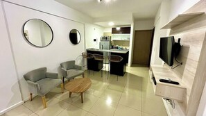 A compact living space with a kitchenette, a dining area with bar stools, a flat-screen TV mounted on the wall, and a round mirror on the wall. - Bright Studio Apartment in the Heart of Palermo (Buenos Aires)