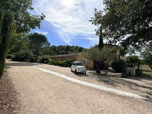 A gravel driveway leading to a white car parked in front of a house with a garden.