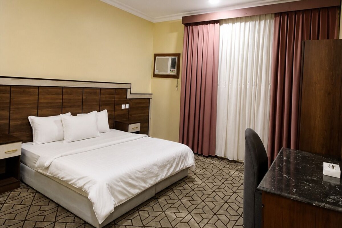 Habitació d'hotel amb llit, escriptori, cadira, armari i finestra amb cortines.