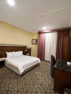 Habitació d'hotel amb llit, escriptori, cadira, armari i finestra amb cortines.