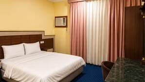 A hotel room with a bed, a desk, a chair, a window with curtains, and a ceiling light. - OrbitNet HJ (Madinah)