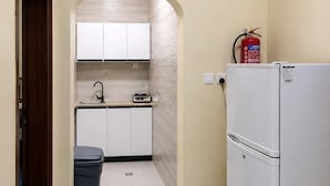 Una cocina estrecha con armarios blancos, un refrigerador blanco y un extintor en la pared.