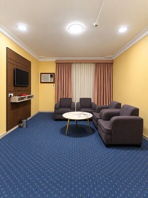 Quarto de hotel com sofá, televisão e mesinha.