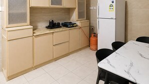 Una cocina compacta con armarios color beige, un refrigerador blanco, una estufa a gas y una mesa de comedor con cubierta de mármol y sillas.