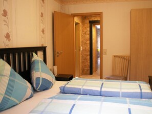 Ein Schlafzimmer mit einem Bett, Kissen, einem Holzkopfende, einem Sessel und einer Tür, die zu einer Steinwand führt.