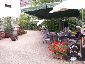 Ein Sitzbereich im Freien mit Tisch und Stühlen, einem grünen Sonnenschirm und Blumentöpfen.