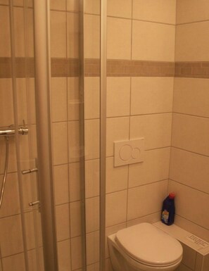 Ein Badezimmer mit Dusche, Toilette und einer Reinigungsflasche auf der Ablagefläche.