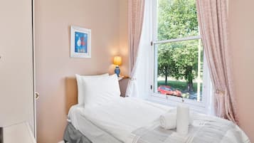 Un dormitorio con una cama, una ventana con cortinas, una lámpara y un cuadro en la pared.