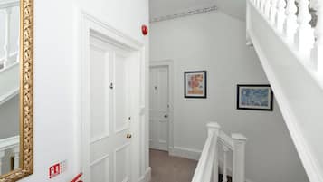 Un pasillo con puertas blancas, un detector de incendios y dos cuadros en la pared.