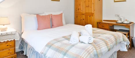 A bedroom with a bed, a wooden wardrobe, a bedside table, a lamp, and a framed picture on the wall.