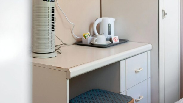 A small kitchenette with a white kettle, a cup, and a tray, a white radiator, and a wooden stool. - Guestready - Links View (Edinburgh)