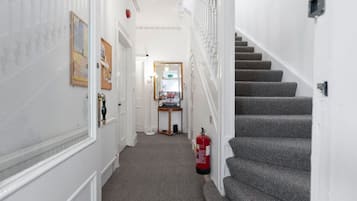 Un couloir doté d’un sol recouvert de moquette, d’un extincteur, d’une porte avec un miroir et d’un escalier dont les marches sont recouvertes de moquette.