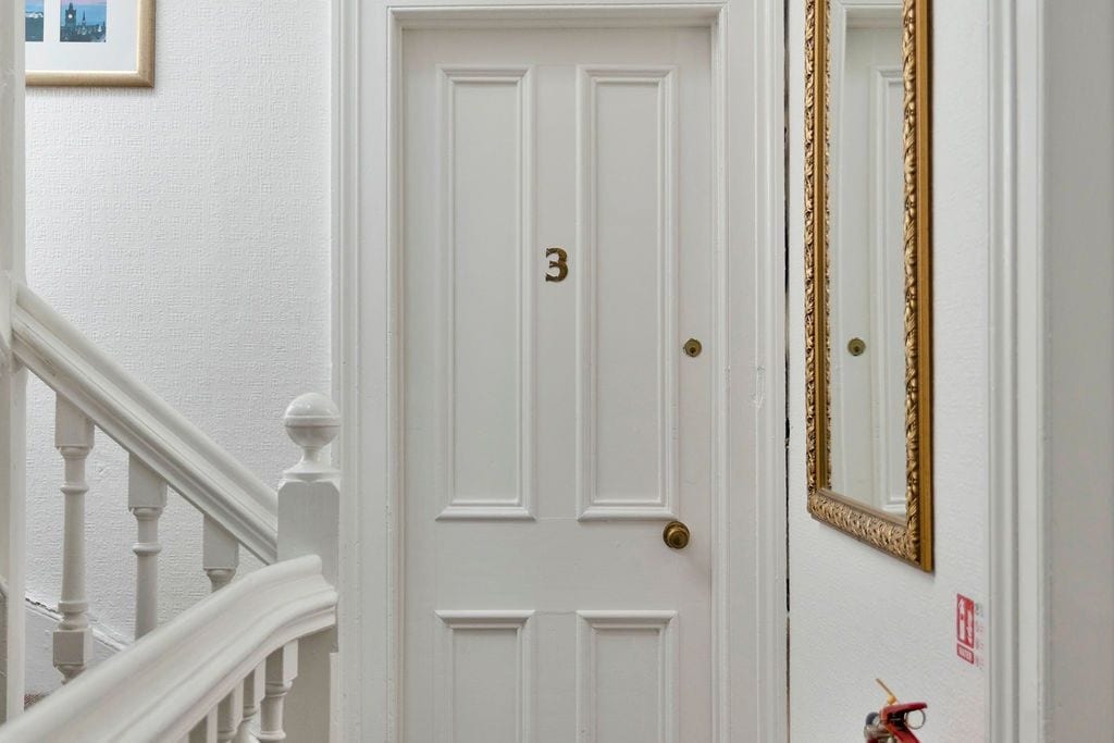 A white door with the number 3, a gold-framed mirror, and a red fire extinguisher on the wall.