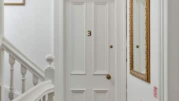 Una puerta blanca con el número 3, un espejo con marco dorado y un extintor rojo en la pared.