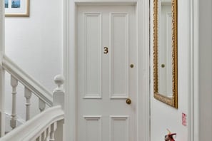 A white door with the number 3, a gold-framed mirror, and a red fire extinguisher on the wall. - Guestready - Links View (Edinburgh)