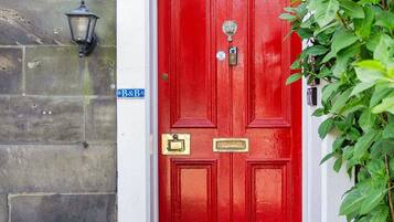 Une porte rouge avec une plaque portant un numéro, un paillasson et une petite plante à côté.