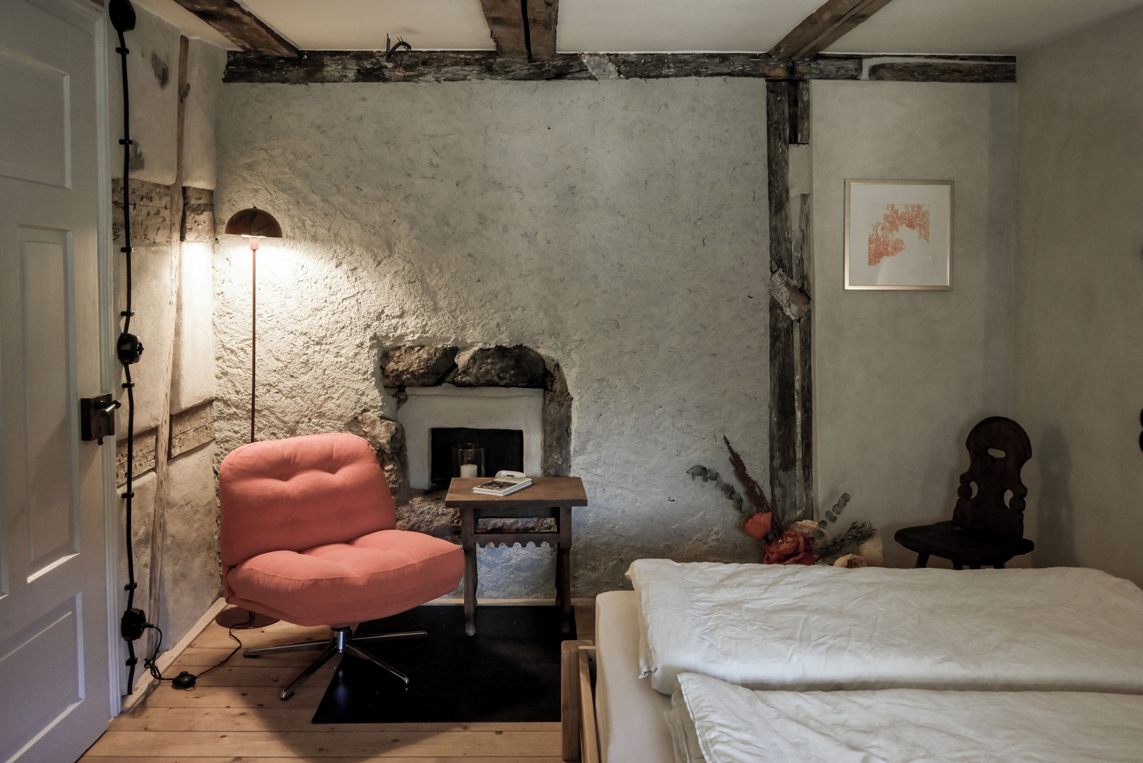 A bedroom with a stone fireplace, a pink chair, a bedside table, and a bed.
