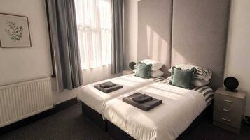 Una habitación de hotel moderna con una cama grande, una mesita de noche, un radiador y una ventana con cortinas.