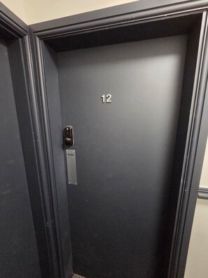 Puerta de ascensor oscura con el número 12, un botón pulsador y una placa metálica con la palabra 'PUSH'.