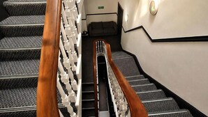 A staircase with a wooden handrail and white balusters, carpeted steps, and a wall-mounted light fixture.