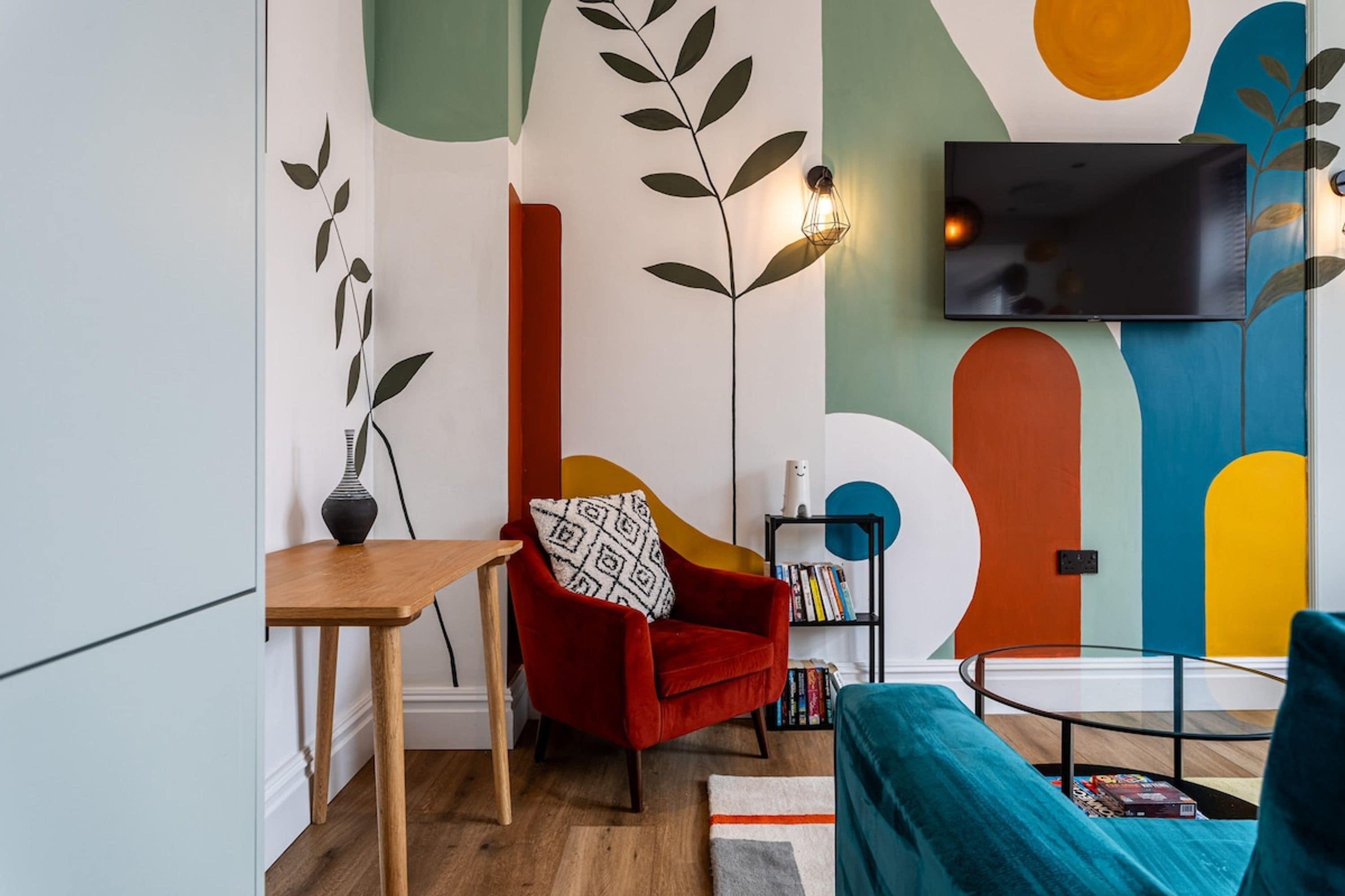 Un salon moderne avec un fauteuil rouge, une petite table, une bibliothèque et un téléviseur à écran plat fixé au mur.
