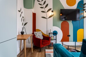 A modern living room with a red armchair, a small table, a bookshelf, and a flat-screen TV mounted on the wall. - Perfect Booking 2 Bed Flat Near Cabot Circus (Bristol)