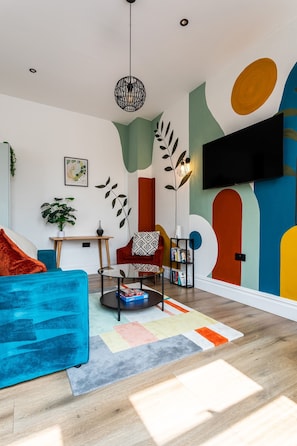 A modern living room with a blue sofa, a red armchair, a coffee table, and a bookshelf. - Perfect Booking 2 Bed Flat Near Cabot Circus (Bristol)