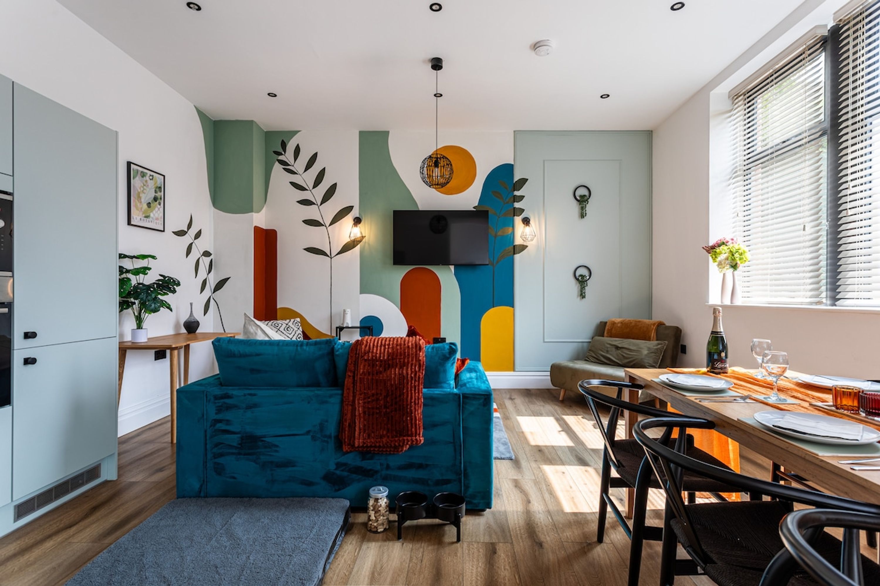 A modern living space with a blue sofa, a dining table set for two, and a kitchen area with a stove.