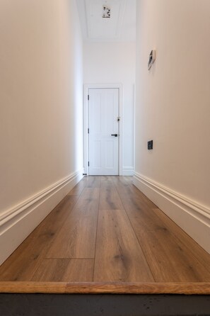 A hallway with a wooden floor, white walls, and a white door at the end. - Perfect Booking 2 Bed Flat Near Cabot Circus (Bristol)