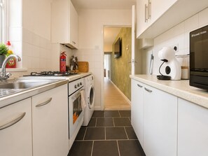 A narrow kitchen with white cabinets, a gas stove, a washing machine, and a coffee machine. - Perfect Booking 2 Bed Home w Street Parking (Coventry)