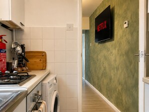 A kitchen with a stove, a washing machine, a wooden cutting board, and a wall-mounted television displaying the Netflix logo. - Perfect Booking 2 Bed Home w Street Parking (Coventry)