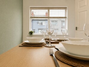 A dining table set with white plates, bowls, and wine glasses, with a window view of buildings in the background. - Perfect Booking 2 Bed Home w Street Parking (Coventry)