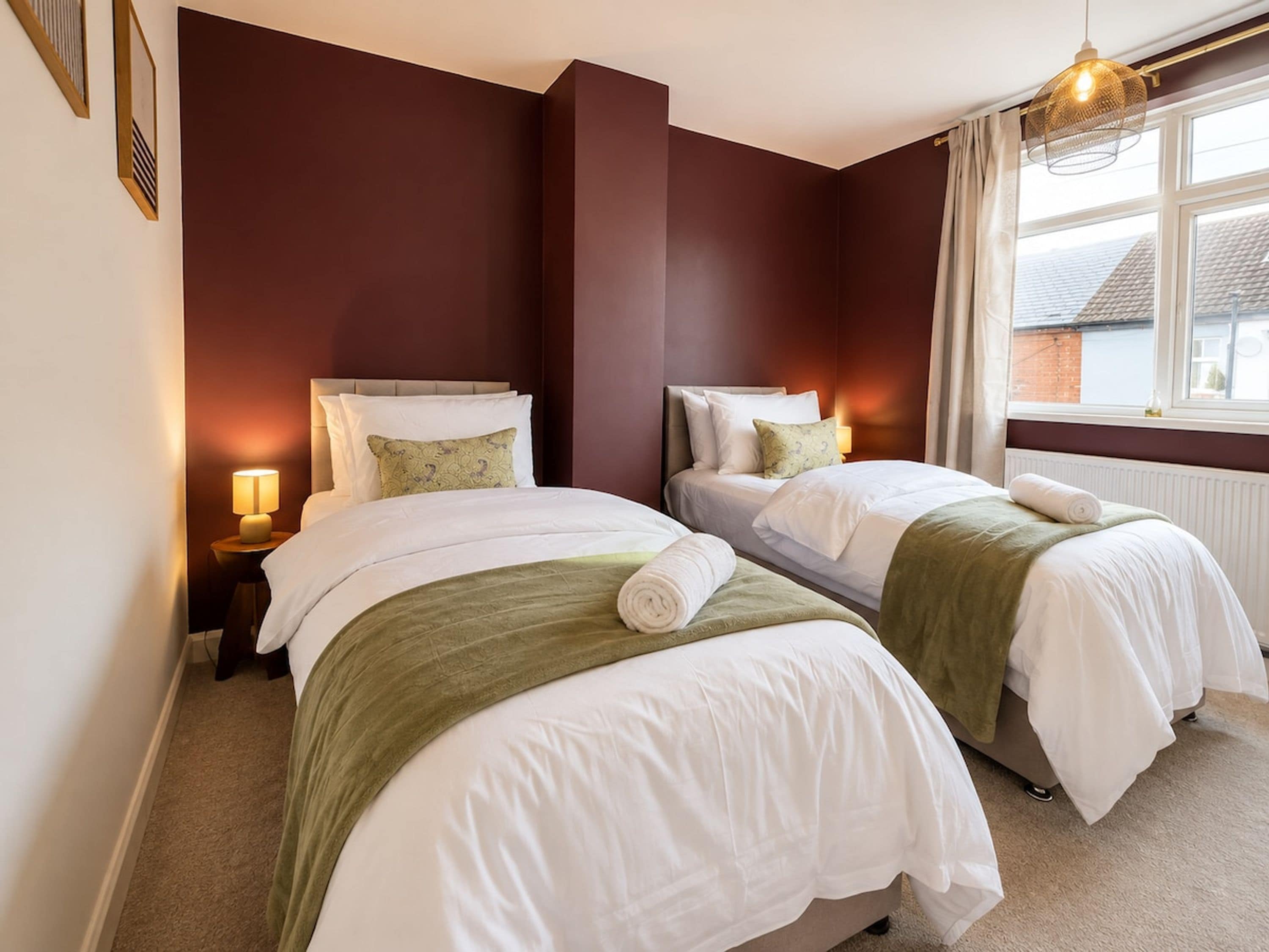 A hotel room with two beds, a window with curtains, and a lamp on each side.