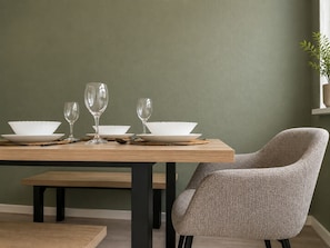 A dining area with a wooden table set for two, a chair, and a green wall. - Perfect Booking 2 Bed Home w Street Parking (Coventry)