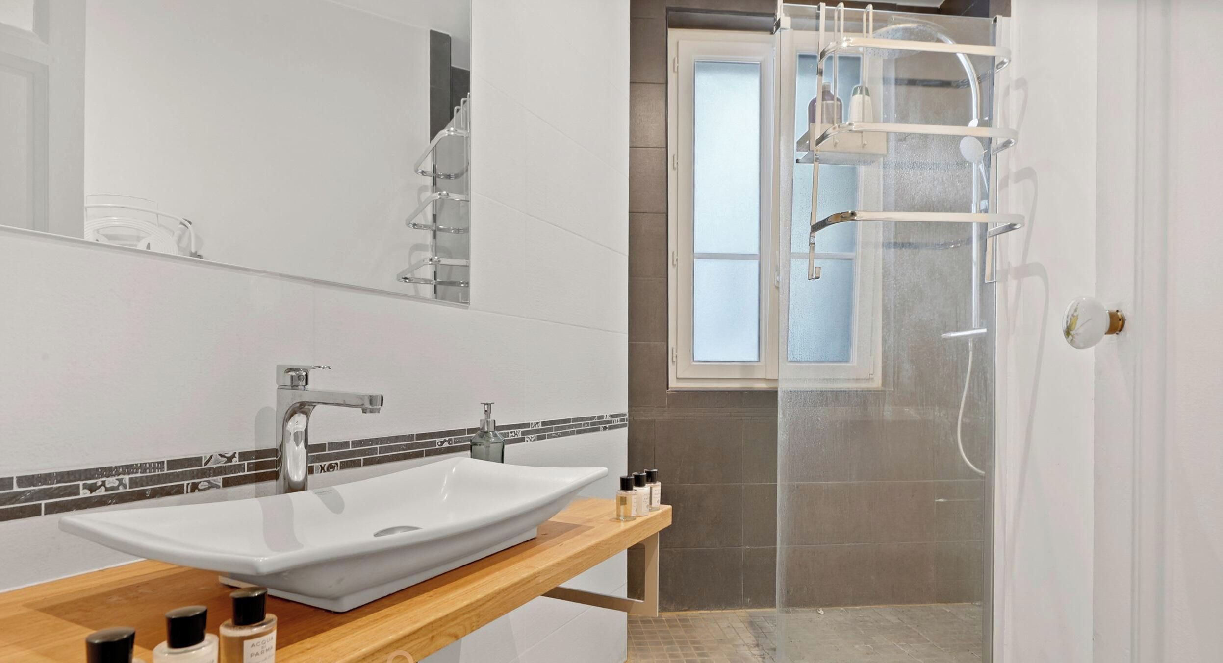 A modern bathroom with a large white sink, a mirror, and a shower area with a glass door.