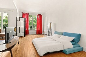 Ein Schlafzimmer mit einem Bett, einem Fernseher, einem Schreibtisch und einem Fenster mit Vorhängen.