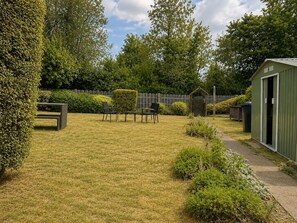 Ein gepflegter Garten mit einer Holzbank, einem kleinen Tisch und einem Gartenhaus.
