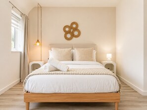 Ein Schlafzimmer mit einem Bett, Nachttischen, einer Wandleuchte und einem Fenster mit Vorhängen.