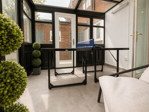 Une véranda avec une porte en verre, une table en métal noir et un canapé blanc.