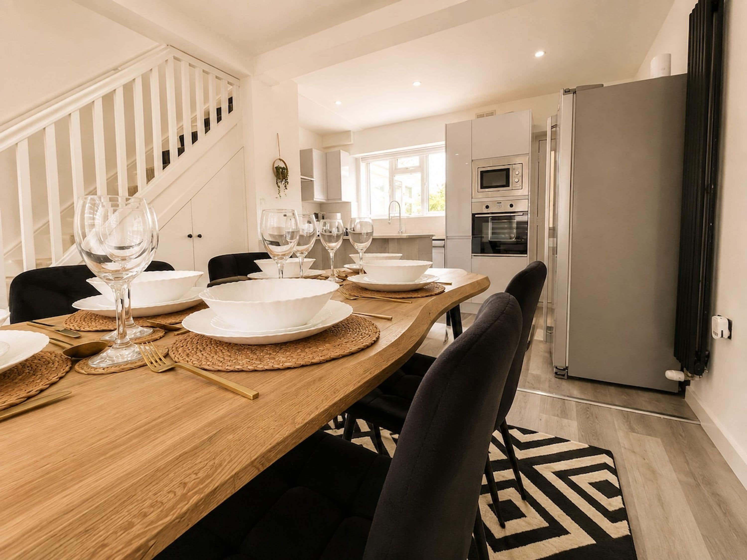 A modern kitchen with a built-in oven, a refrigerator, and a dining area with a wooden table set for a meal.