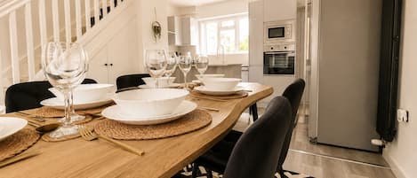 A modern kitchen with a built-in oven, a refrigerator, and a dining area with a wooden table set for a meal.