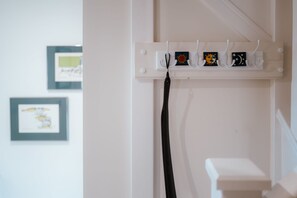 Pared branca com prateleira branca exibindo quatro pequenas obras de arte emolduradas e uma tira preta pendurada abaixo.
